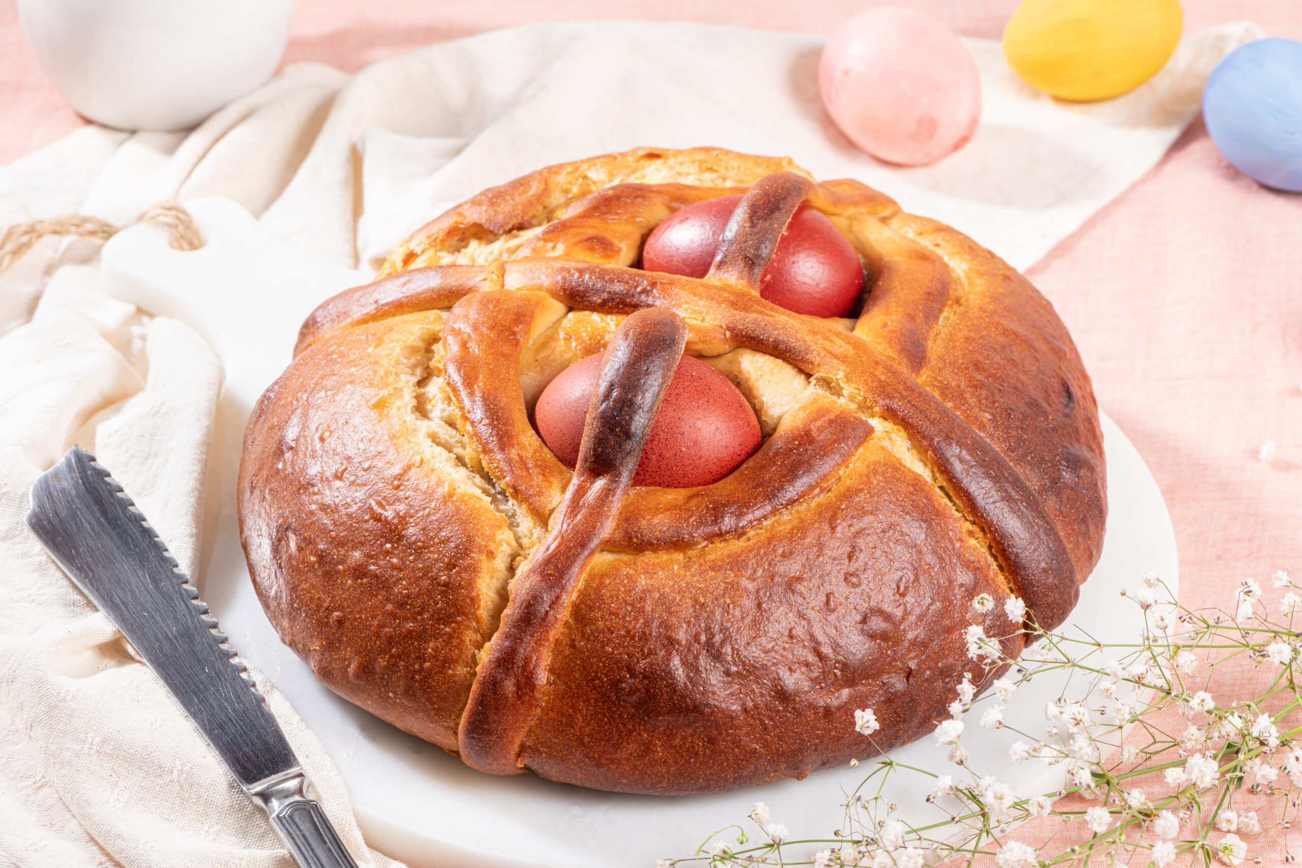 Portuguese traditional Easter cake. Folar with eggs on easter table. Blossom flowers and colorful painted eggs